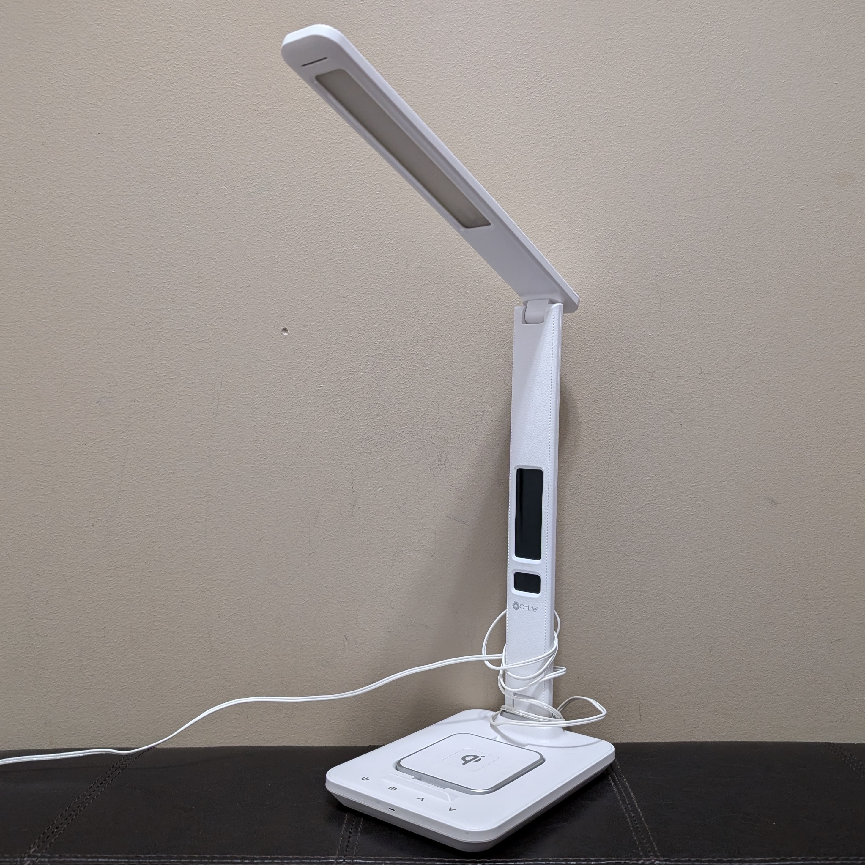 A desk lamp with a digital clock and a charging pad.